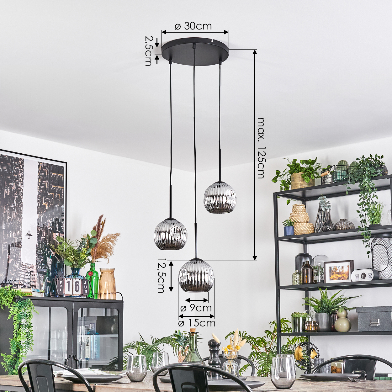 Drei Pendelleuchten mit Glaskugeln hängen über einem Tisch. Ein schwarzes Regal mit Pflanzen und ein Schrank mit Dekoration sind im Hintergrund.