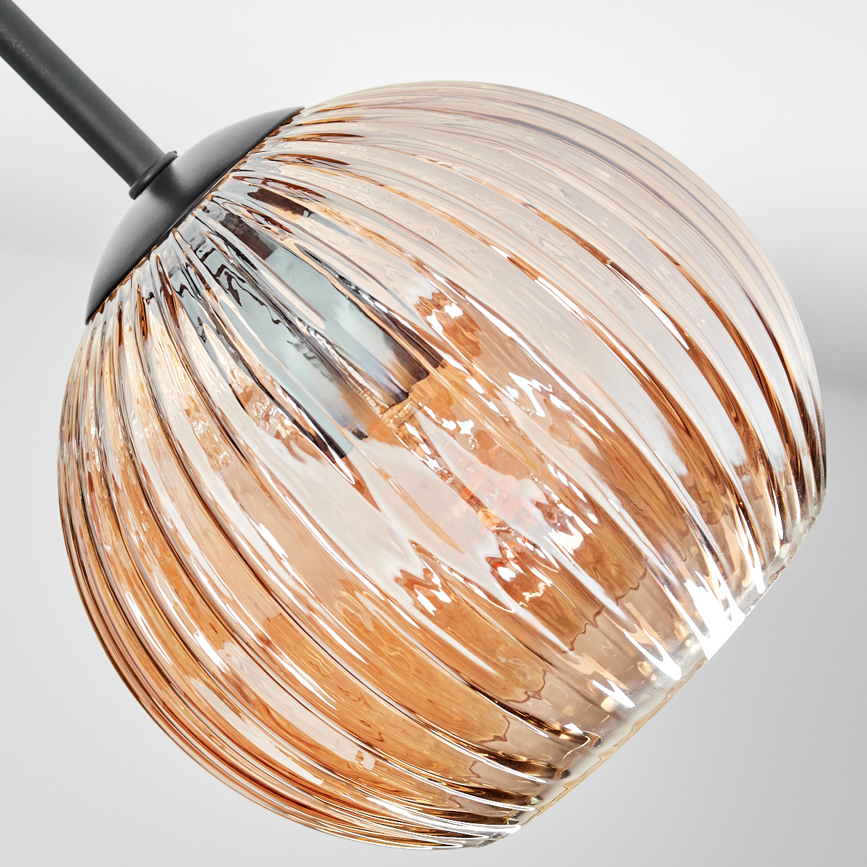 Nahaufnahme einer Glasleuchte. Das klare Glas hat ein geripptes Design. Die Leuchte ist bernsteinfarben und hat eine schwarze Metallhalterung.