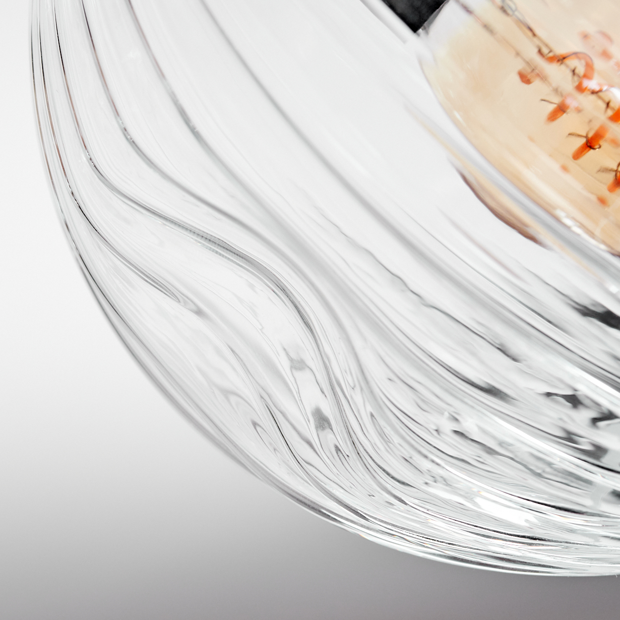 Nahaufnahme einer durchsichtigen Glasschale mit gewelltem Design. Im Hintergrund ist eine zweite Schale mit orangefarbenen Dekorationen zu sehen.
