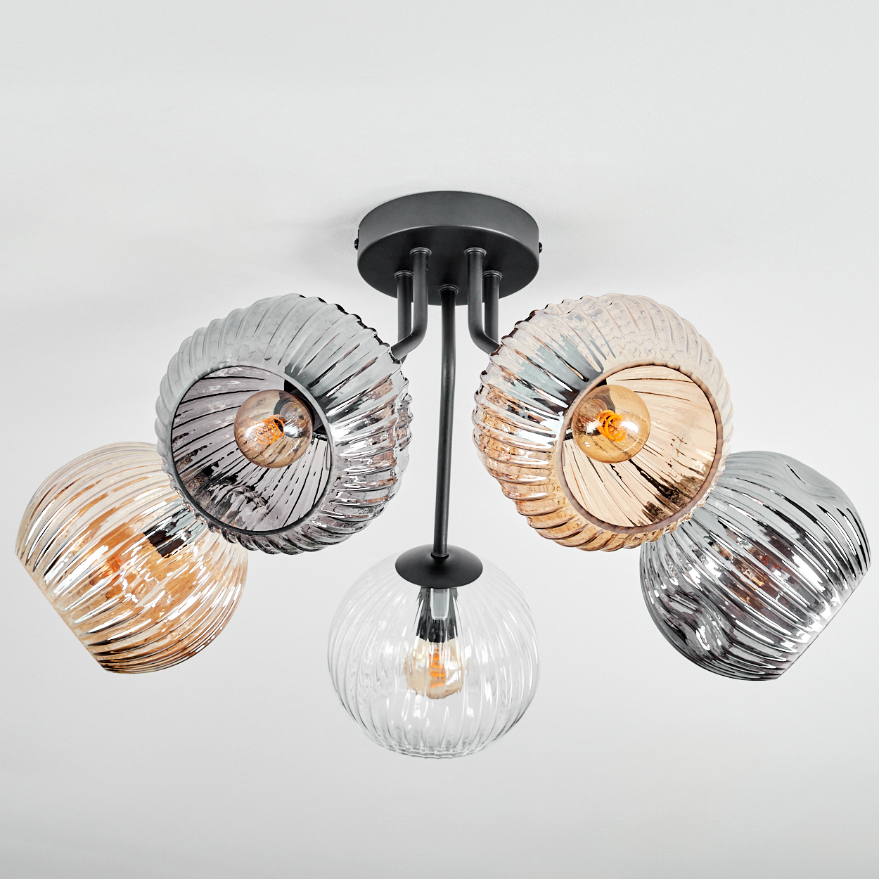 Eine moderne Deckenlampe mit fünf Glasschirmen. Einige sind klar, andere silber- oder bernsteinfarben, mit Glühbirnen.
