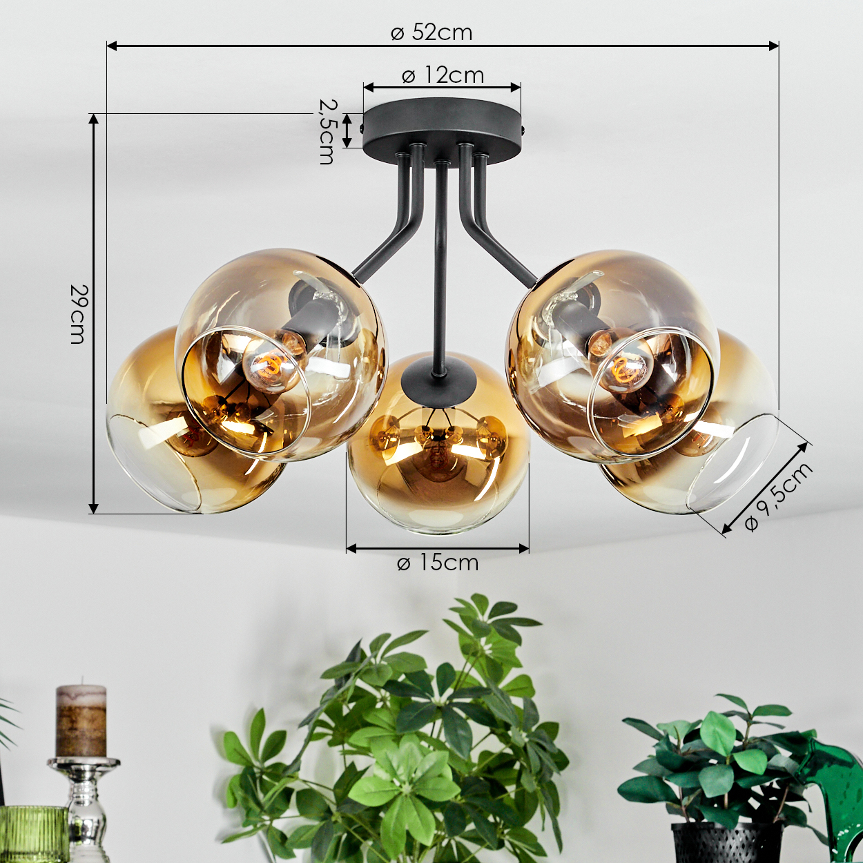 Eine moderne Deckenlampe mit fünf Glaskugeln in Bernsteinfarbe und schwarzer Metallstruktur. Pflanzen sind im Vordergrund.