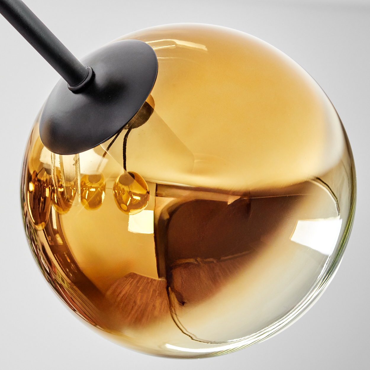 Nahaufnahme einer Glaskugel-Lampe. Die Kugel ist bernsteinfarben. Eine schwarze Halterung und Stütze sind sichtbar. Reflexionen sind vorhanden.