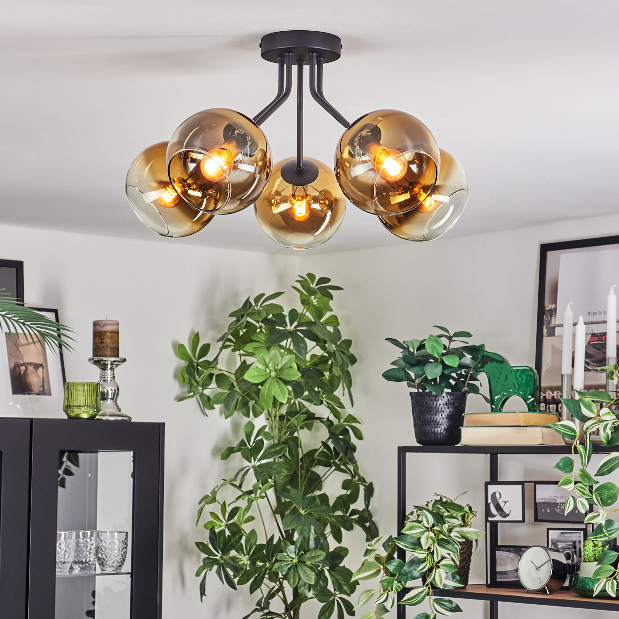 Ein modernes Wohnzimmer mit schwarzer Deckenlampe mit goldenen Glasschirmen. Pflanzen und Möbel sind im Raum.