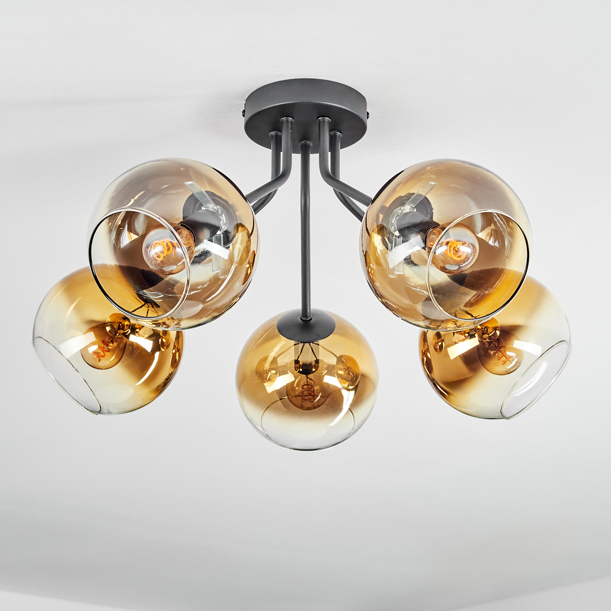 Moderne Deckenleuchte mit fünf bernsteinfarbenen Glaskugeln, die an einem dunkelgrauen Metallrahmen hängen, vor einer weißen Decke.