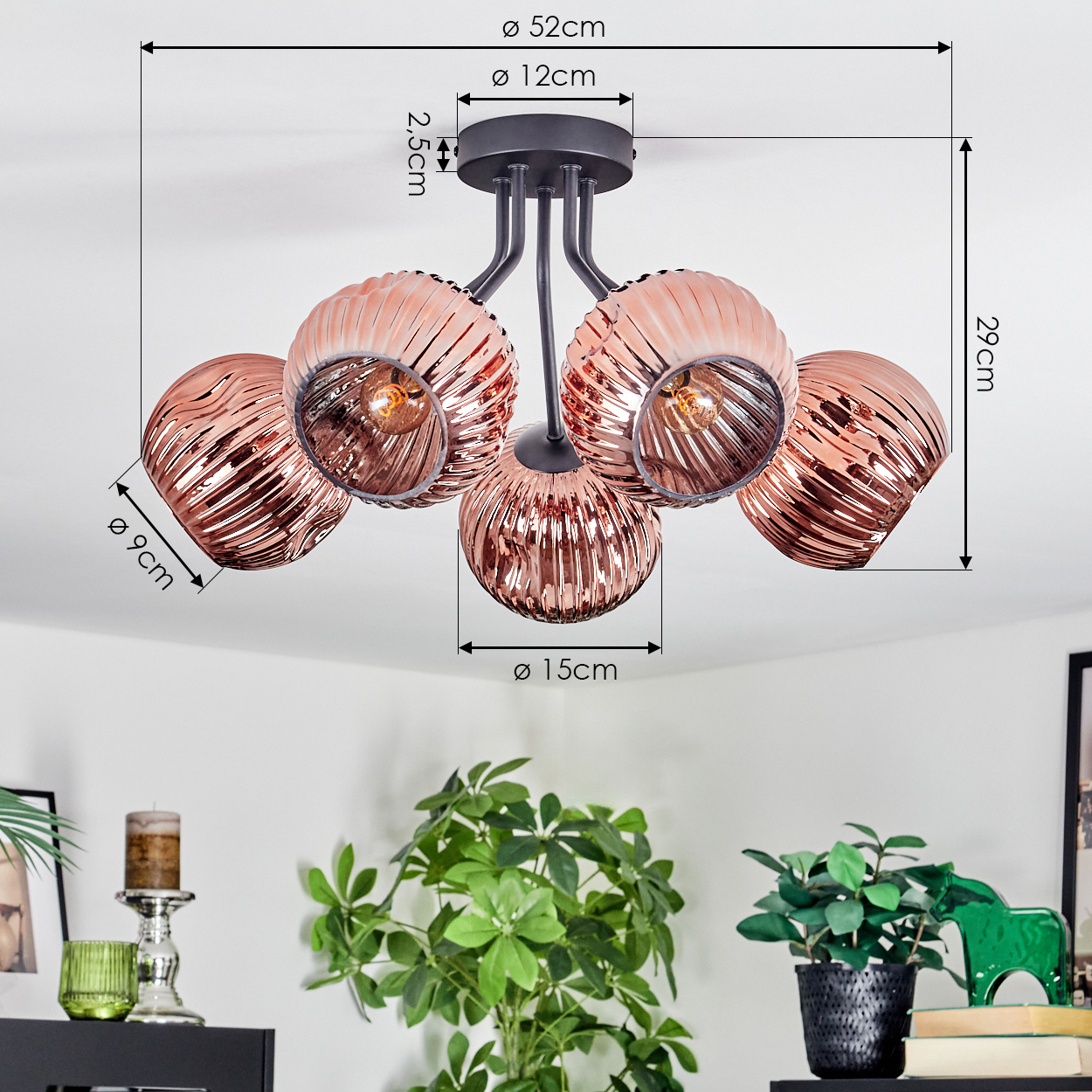 Eine moderne Deckenlampe mit fünf kupferfarbenen Glasschirmen, Maße sind angegeben. Pflanzen und Dekorationsartikel im Hintergrund.