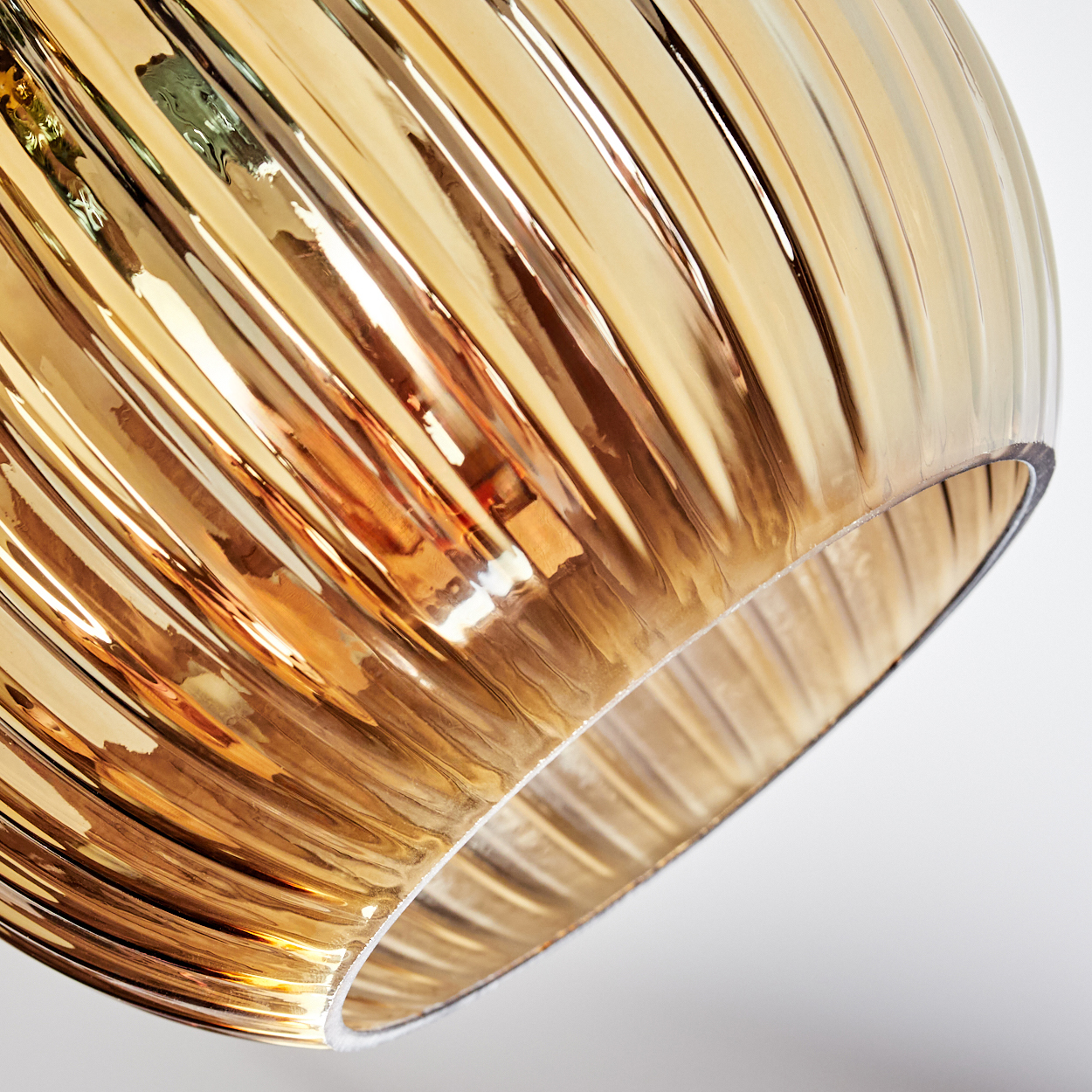 Nahaufnahme eines Glasschirms. Er ist gerippt und hat einen goldbraunen Farbton. Der Hintergrund ist weiß.