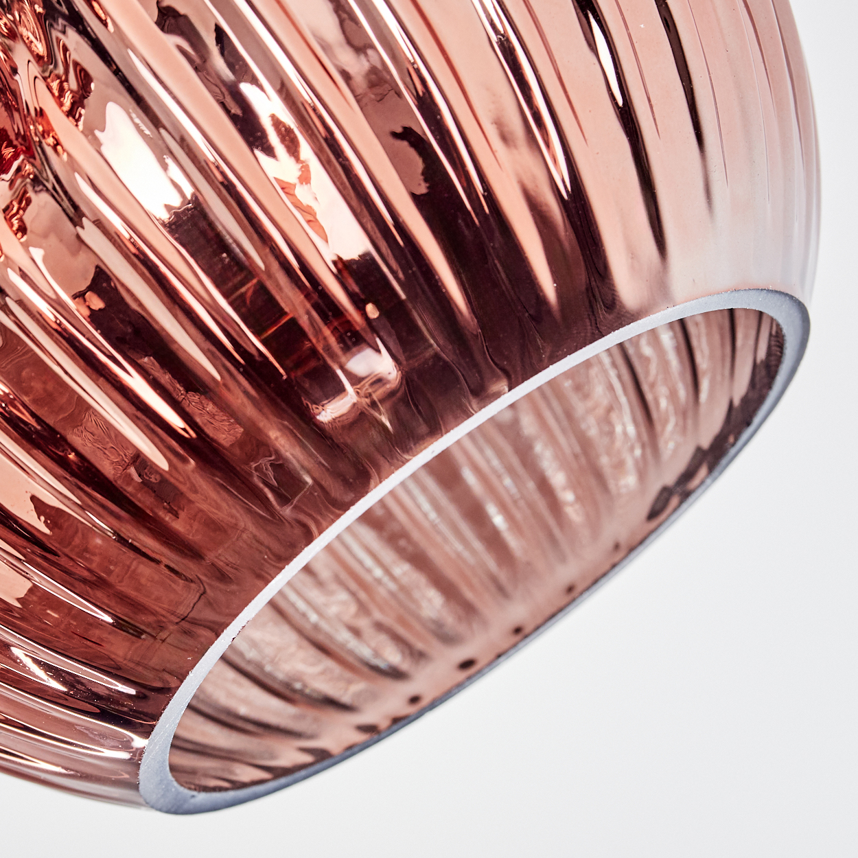 Nahaufnahme eines roségoldenen, gerippten Glasschirms vor weißem Hintergrund. Der Rand ist weiß.