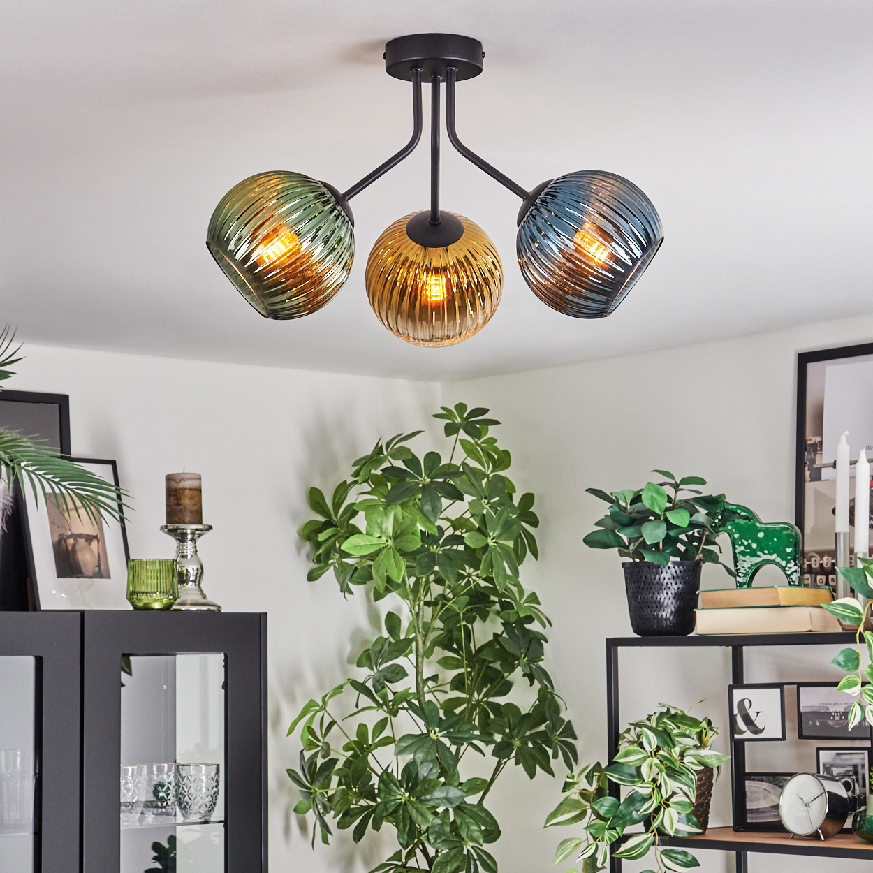 Deckenlampe mit drei farbigen Glaskugeln. Pflanzen und Möbel im Vordergrund, Bilder und Dekoration im Hintergrund.