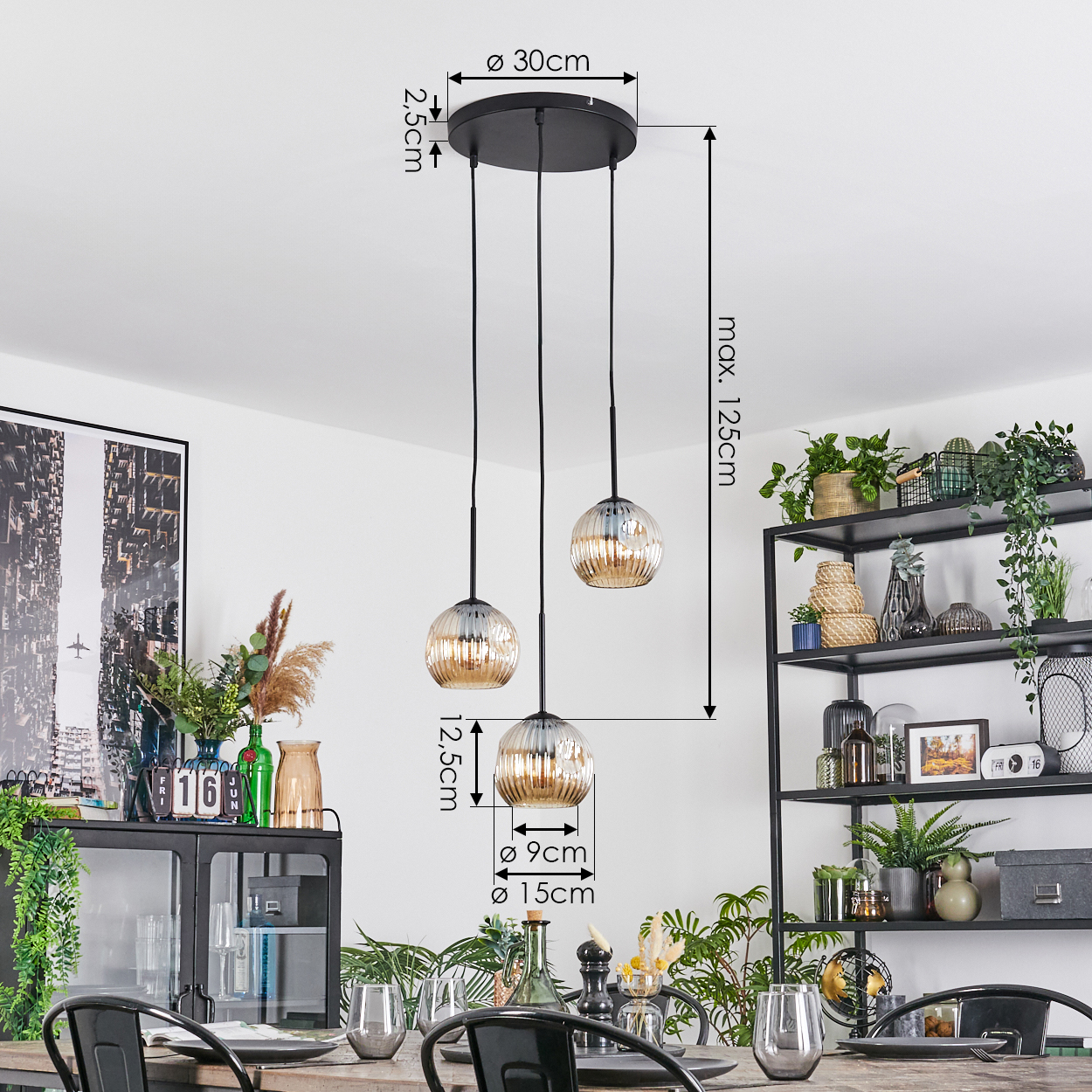 Drei Pendelleuchten mit Glaskugeln hängen über einem Tisch. Im Hintergrund ein Regal mit Pflanzen und Dekoration.