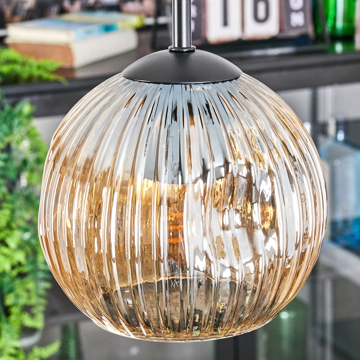 Nahaufnahme einer Glaskugel-Pendelleuchte mit geripptem Design. Sie hängt an einer schwarzen Halterung. Der Hintergrund ist unscharf.