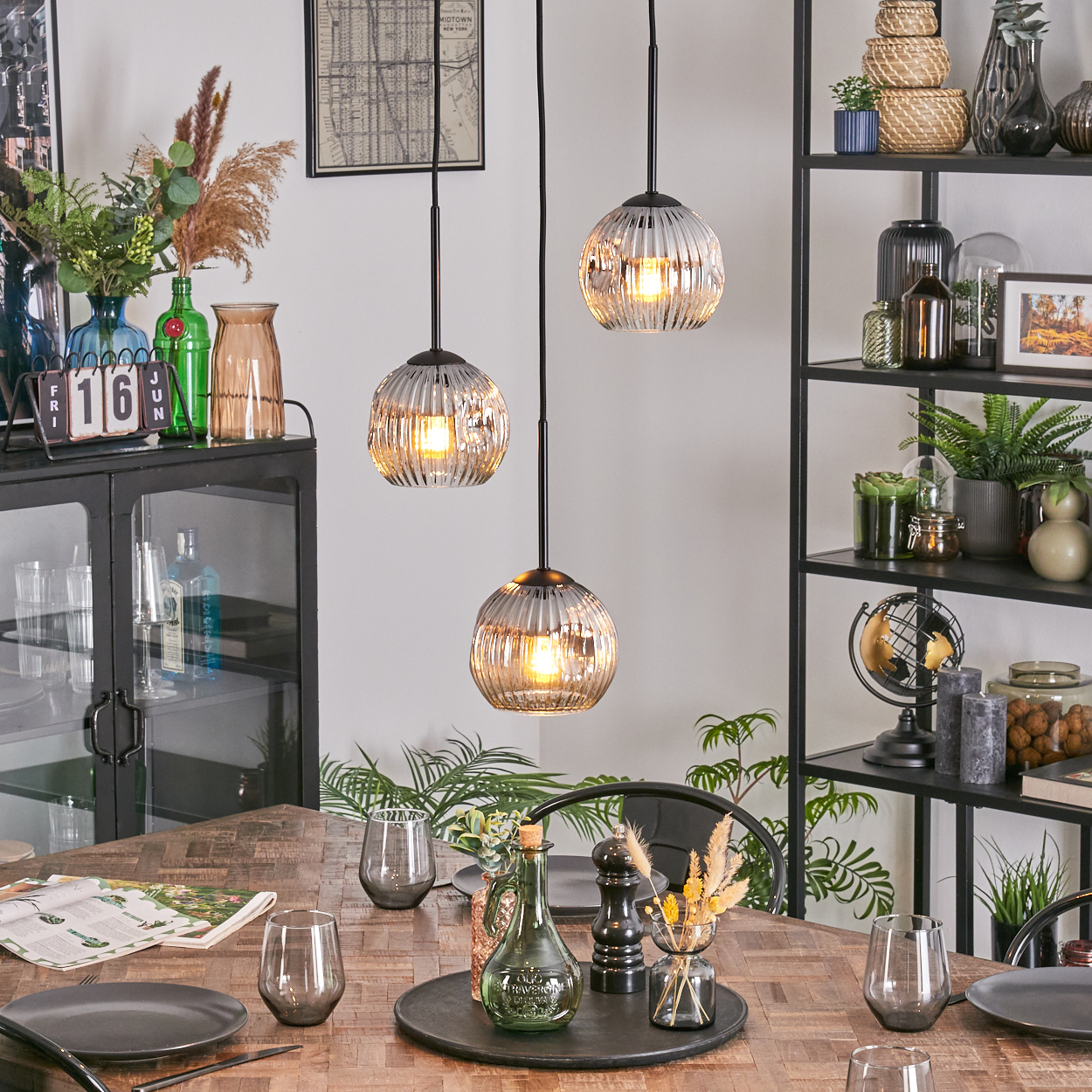 Esszimmer mit Holztisch, Glaslampen und Dekorationsartikeln. Enthält Pflanzen, Gläser und ein schwarzes Metallregal.