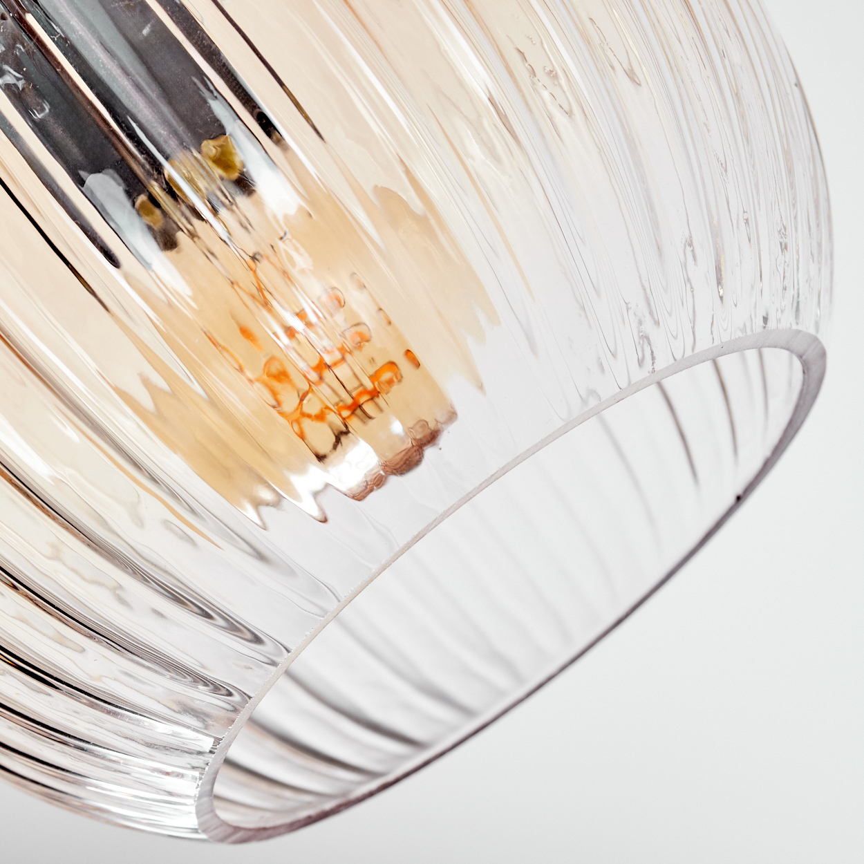 Nahaufnahme eines Lampenschirms aus Glas mit geripptem Design. Im Inneren ist eine orangefarbene Glühbirne zu sehen. Der Hintergrund ist weiß.