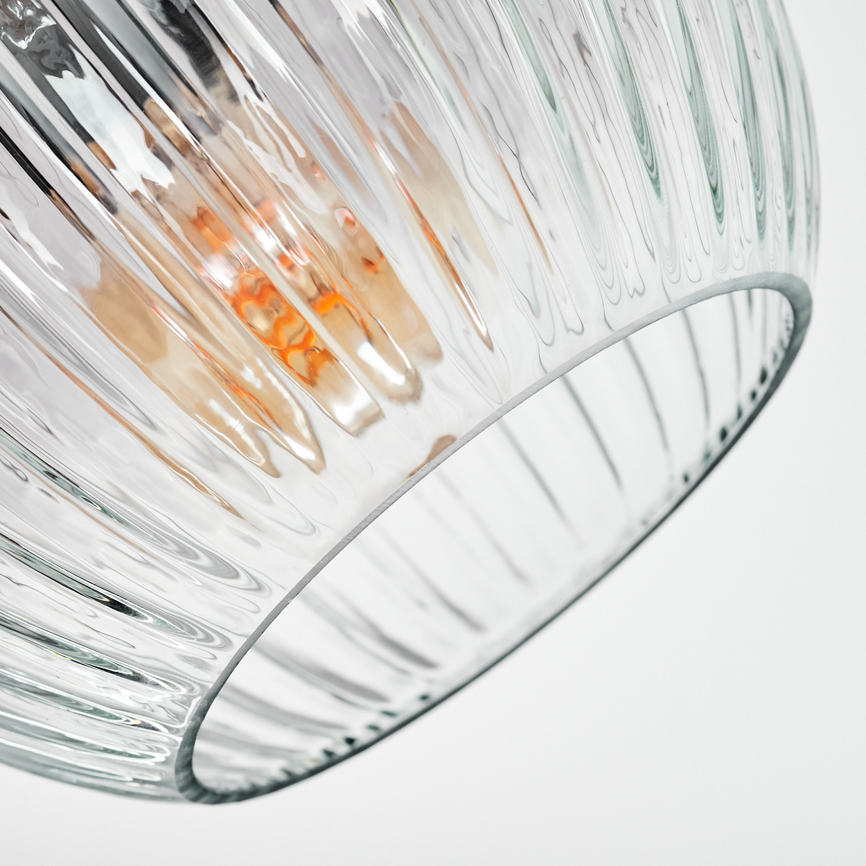 Nahaufnahme eines Lampenschirms aus klarem Glas mit gerippter Textur, der eine warme Glühbirne zeigt, vor weißem Hintergrund.