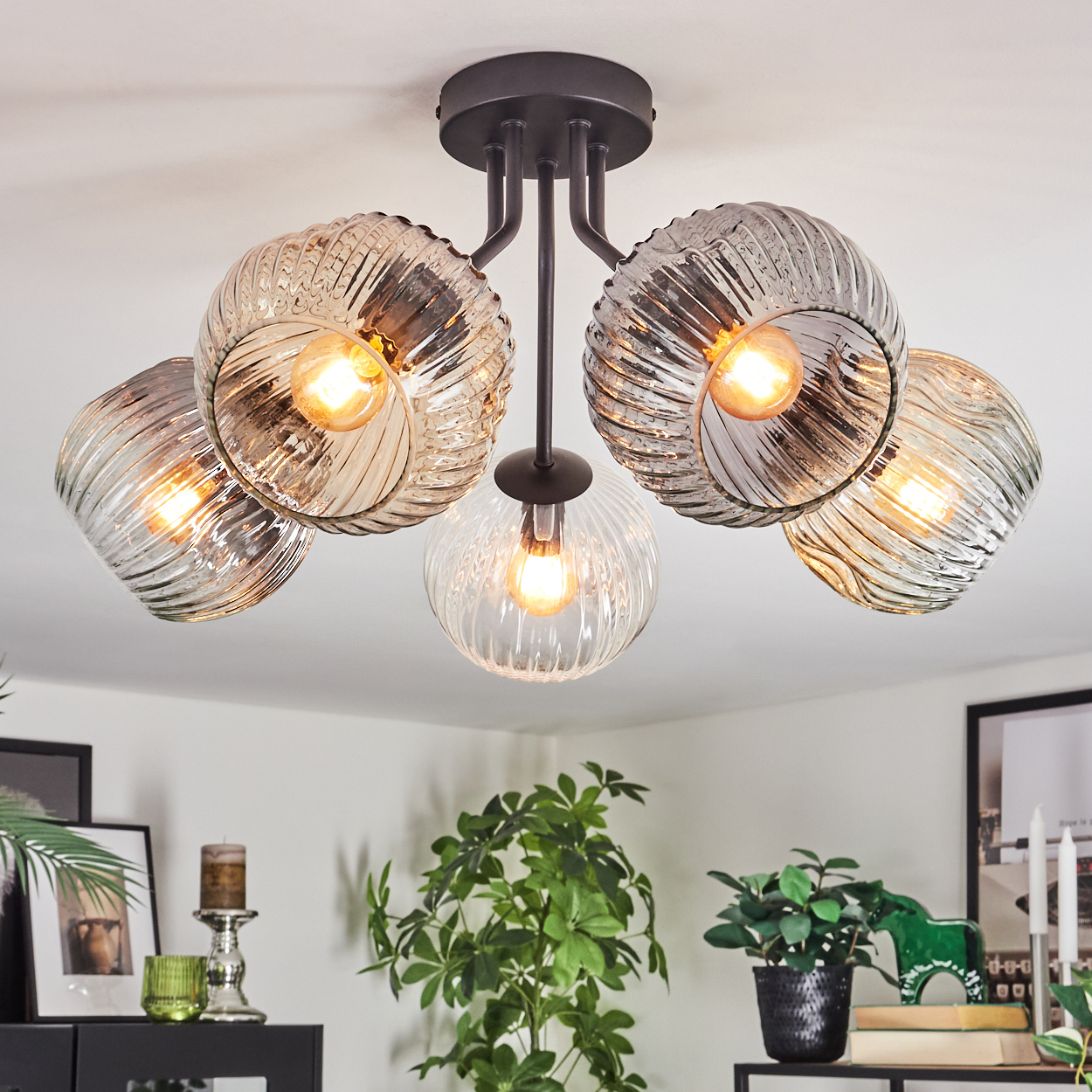Eine moderne Deckenlampe mit fünf Glaskugeln, jede mit einer leuchtenden Glühbirne. Der Raum hat Dekor und Pflanzen.
