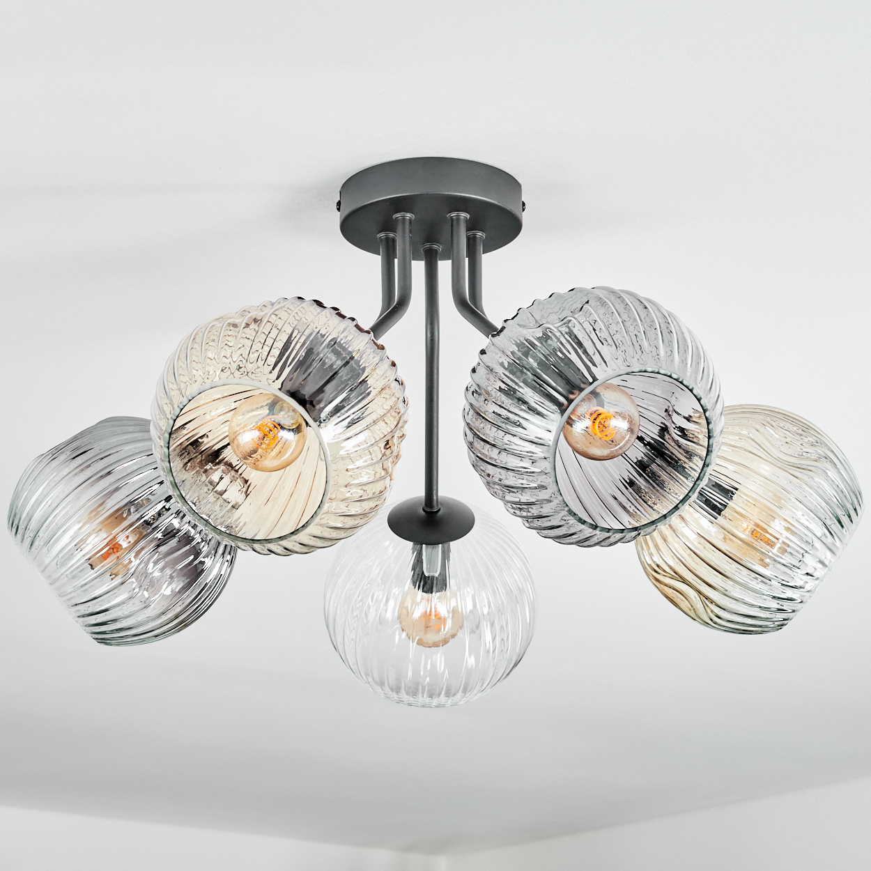 Eine moderne Deckenleuchte mit fünf Glasschirmen und freiliegenden Glühbirnen. Die Leuchte hat ein dunkles Metallfinish vor weißem Hintergrund.