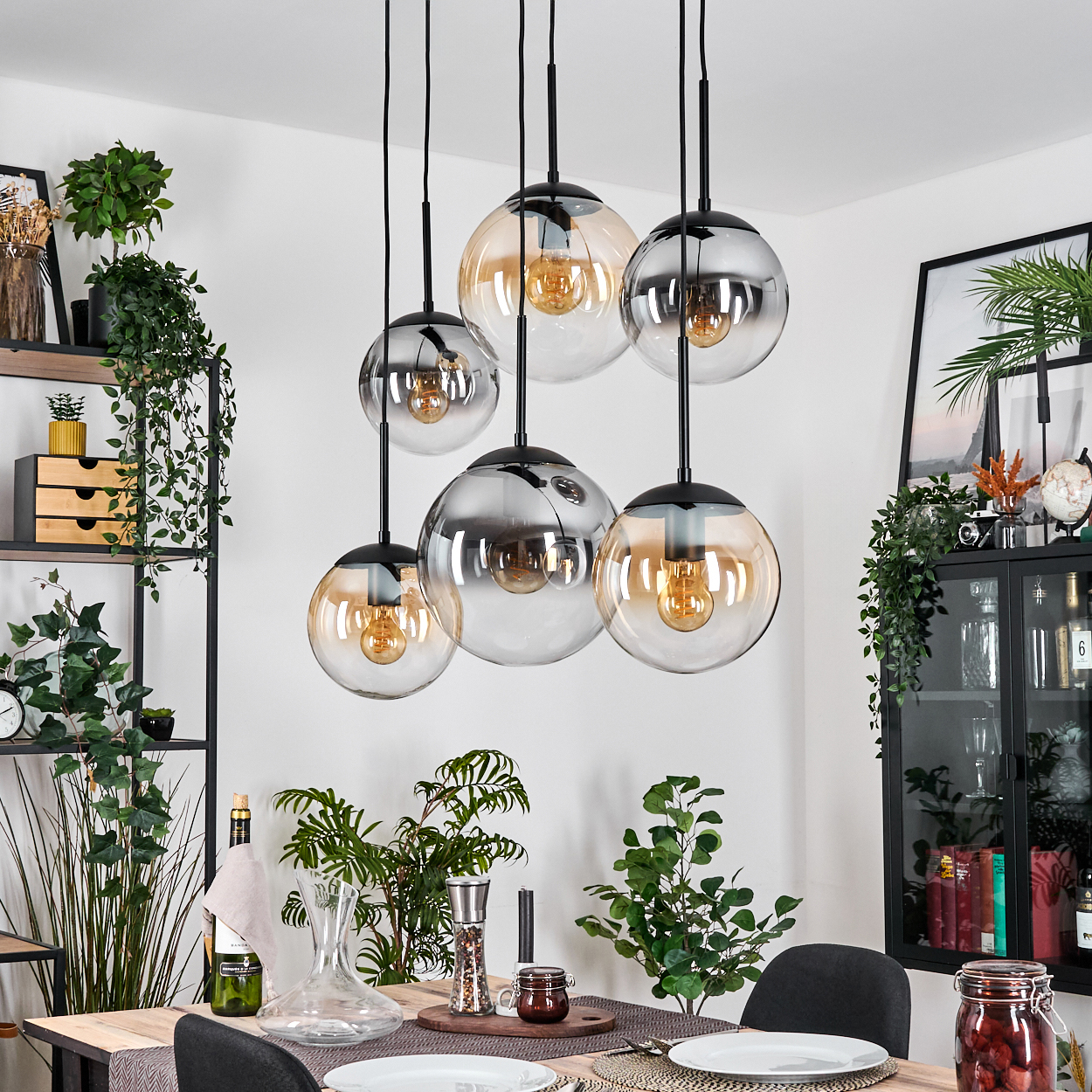 Esszimmer mit Tisch, Stühlen und Hängeleuchten. Pflanzen und Dekorationen sind ebenfalls im Raum zu sehen.