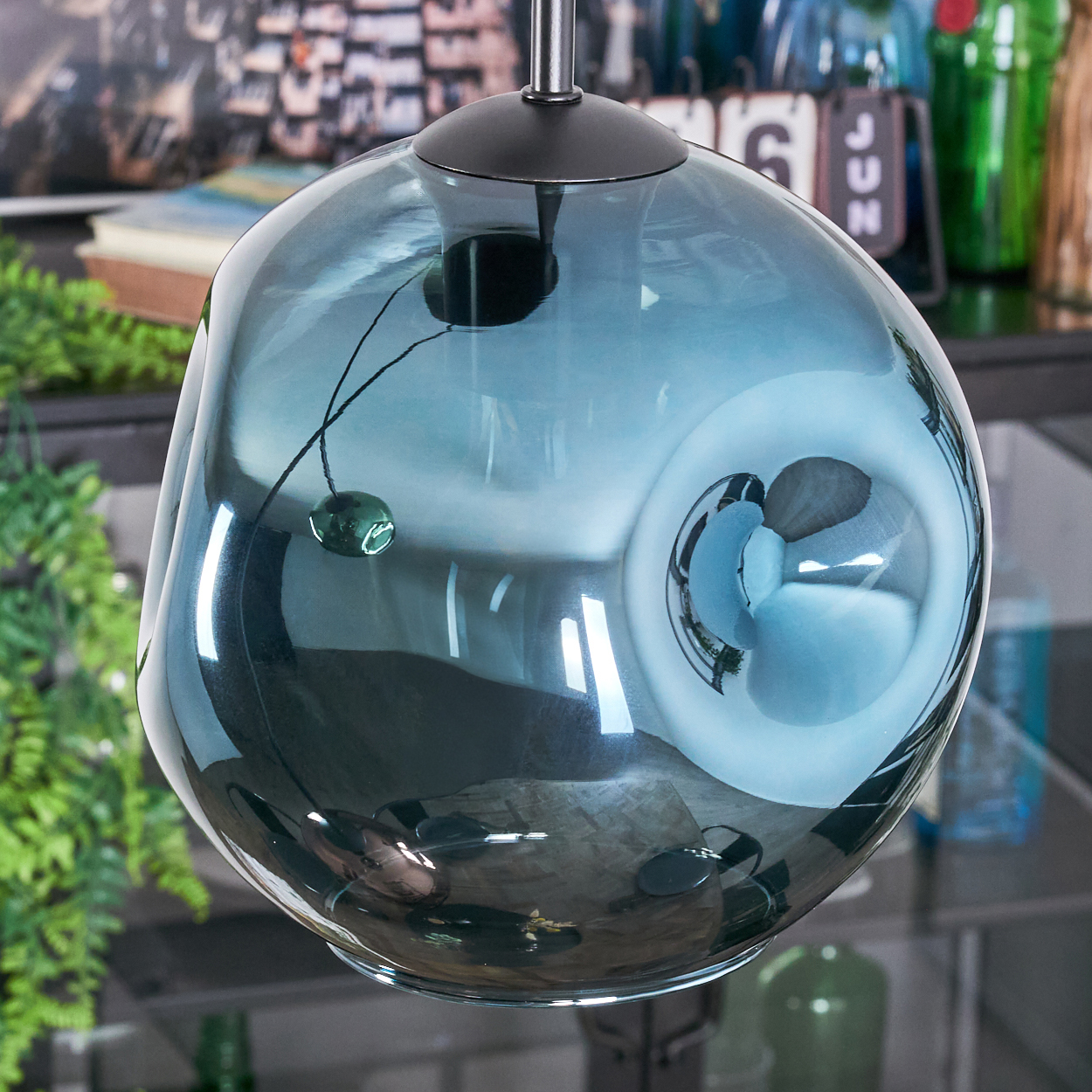 Eine blaue Glas-Pendelleuchte mit einzigartiger Form hängt von der Decke. Reflexionen und andere Objekte sind im Glas sichtbar.