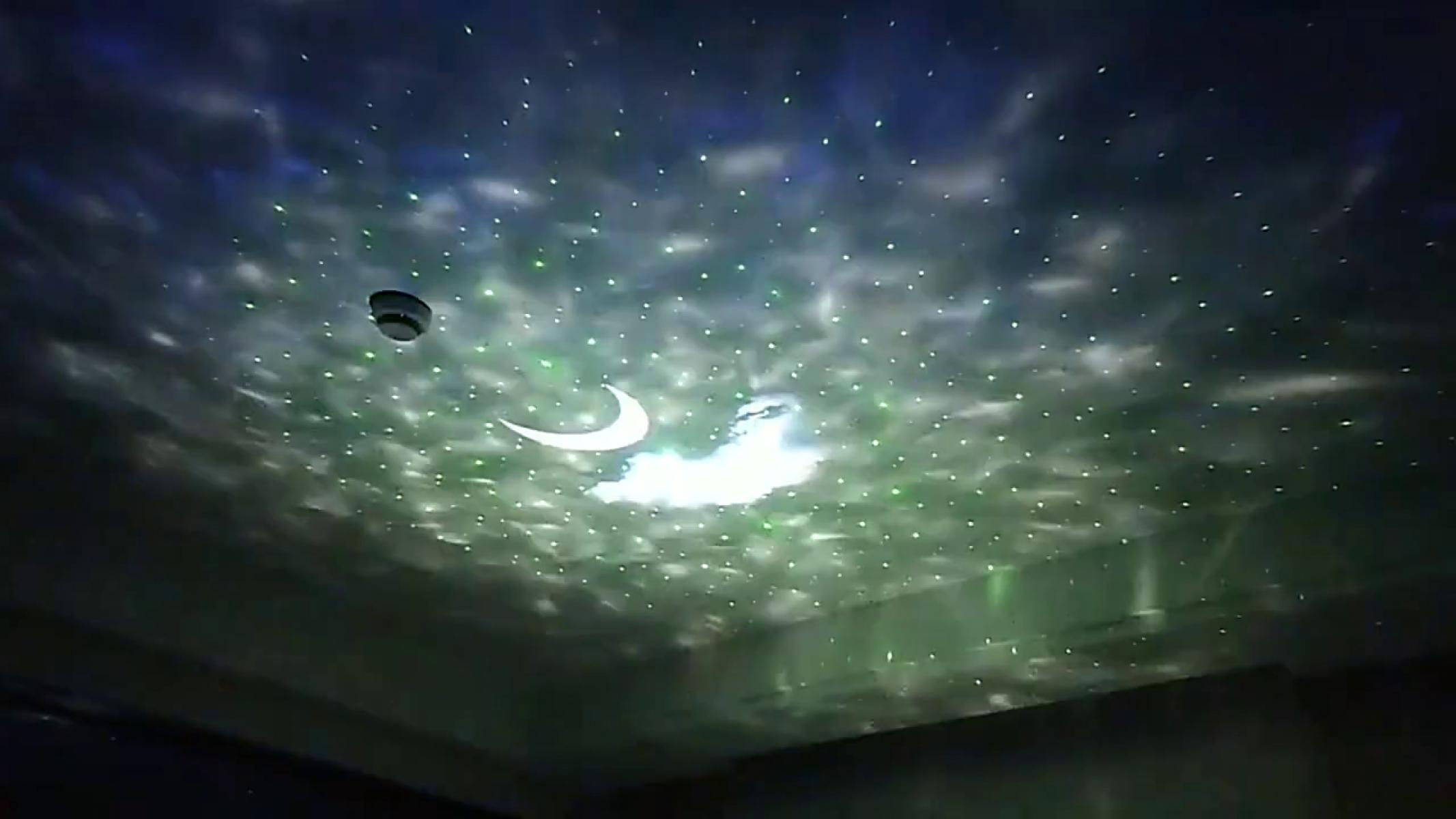 Deckenprojektion von Sternen, Mond und Wolken. Ein Rauchmelder ist sichtbar. Die Farben sind Grün, Weiß und Blau.