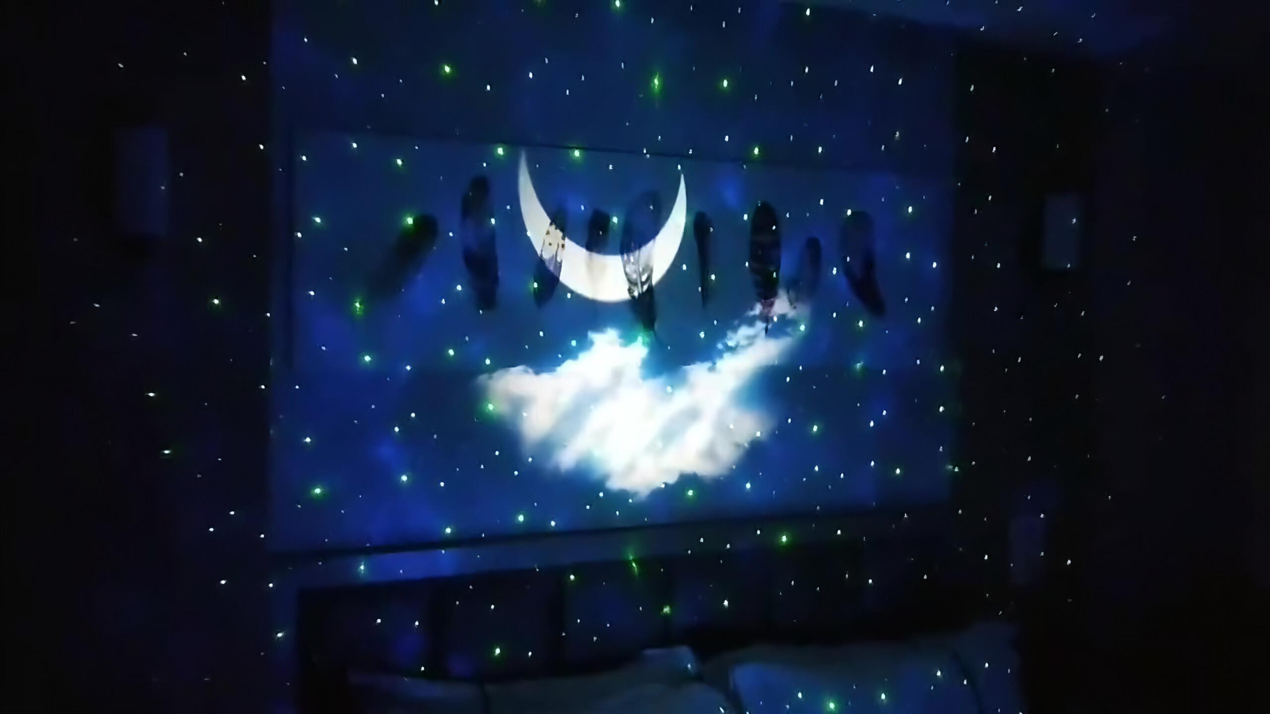 Eine Nachtszene mit Mond, Wolken und Sternen an der Wand. Grüne und weiße Lichter erzeugen den Effekt.
