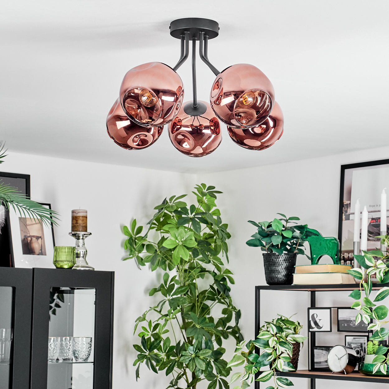 Eine moderne Deckenlampe mit kupferfarbenen Glaskugeln. Der Raum hat Pflanzen, schwarze Möbel und gerahmte Bilder.