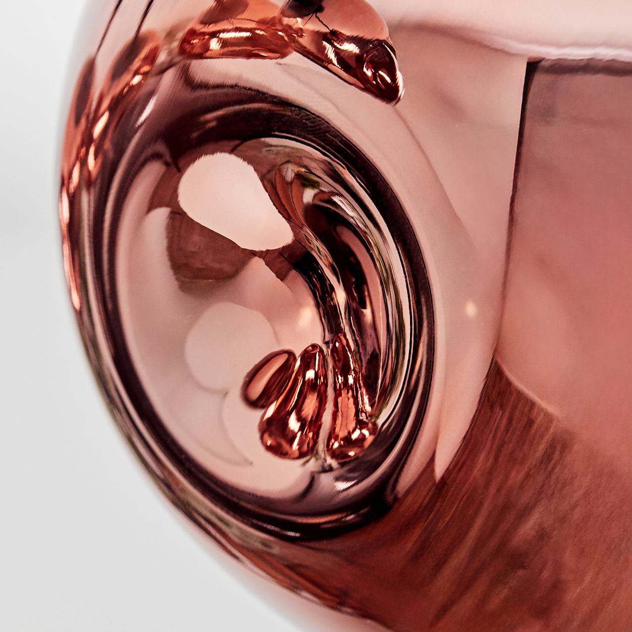 Nahaufnahme eines reflektierenden, roségoldfarbenen Objekts mit gebogenen Oberflächen. Reflexionen und Wirbel tragen zur Abstraktheit bei.