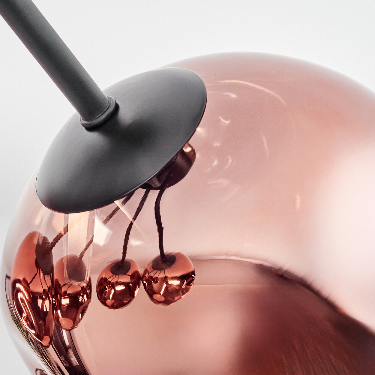 Nahaufnahme einer modernen Lampe. Sie hat eine kupferfarbene Glaskugel, einen schwarzen Stiel und dekorative kirschartige Elemente.