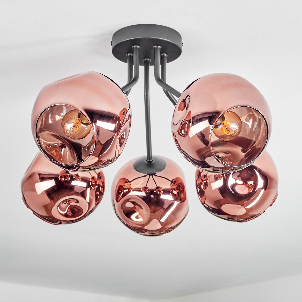 Eine moderne Deckenlampe mit fünf kupferfarbenen, kugelförmigen Schirmen, die jeweils eine Glühbirne enthalten, vor einer weißen Decke.
