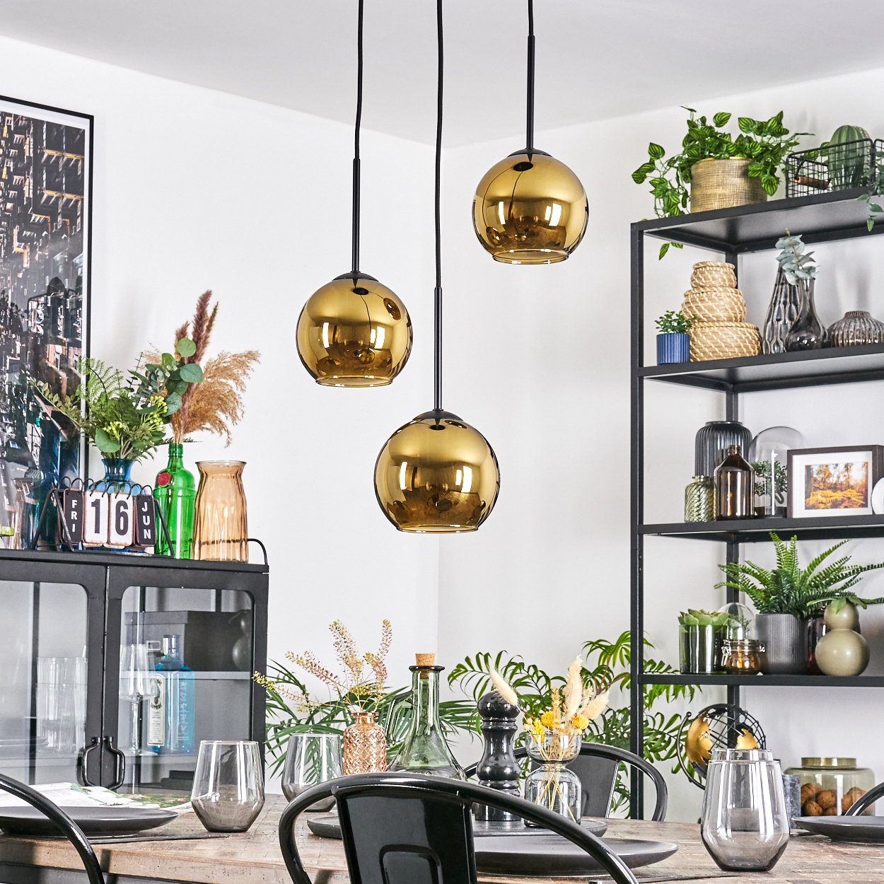 Esszimmer mit goldenen Pendelleuchten. Tisch mit Gläsern gedeckt. Regale mit Pflanzen und Dekor.
