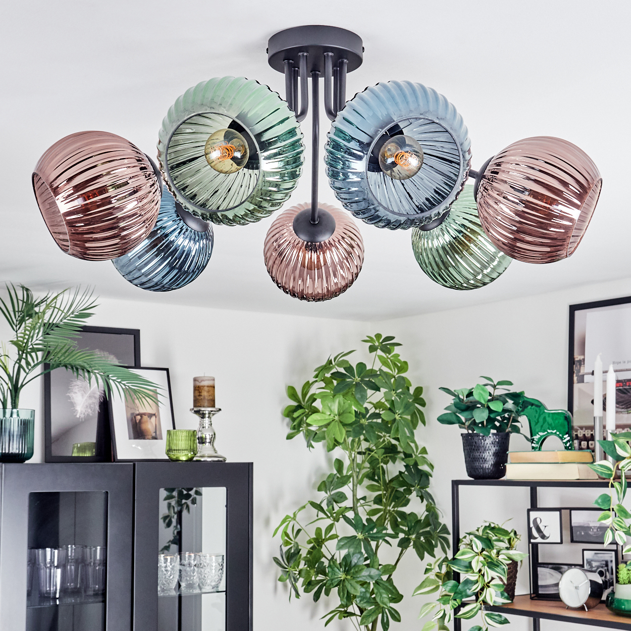 Eine moderne Deckenleuchte mit sechs bunten Glaskugeln hängt über einem Wohnzimmer mit Pflanzen und Dekoration.