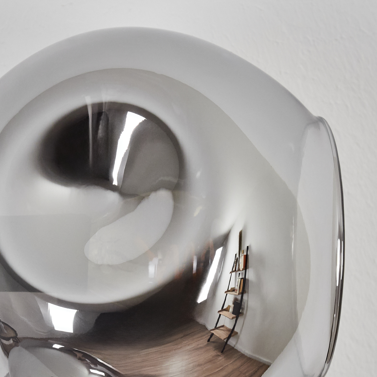 Ein großes, reflektierendes, graues Glasobjekt. Innen spiegeln sich eine kleine Leiter und Bücher vor weißer Wand und Holzboden.