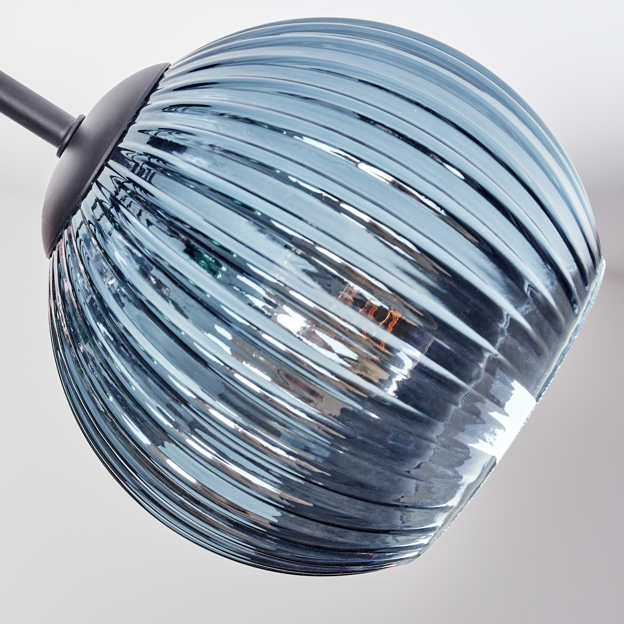 Nahaufnahme eines blauen Glasschirmes mit gerippter Textur. Der Hintergrund ist weiß. Die Lampe ist beleuchtet.