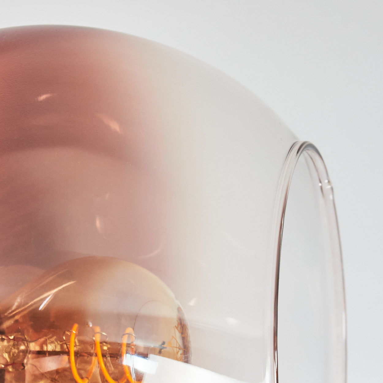 Nahaufnahme einer Leuchte mit einer Glühbirne in einem klaren, glockenförmigen Glas. Das Glas hat einen Farbverlauf von rosa nach weiß.