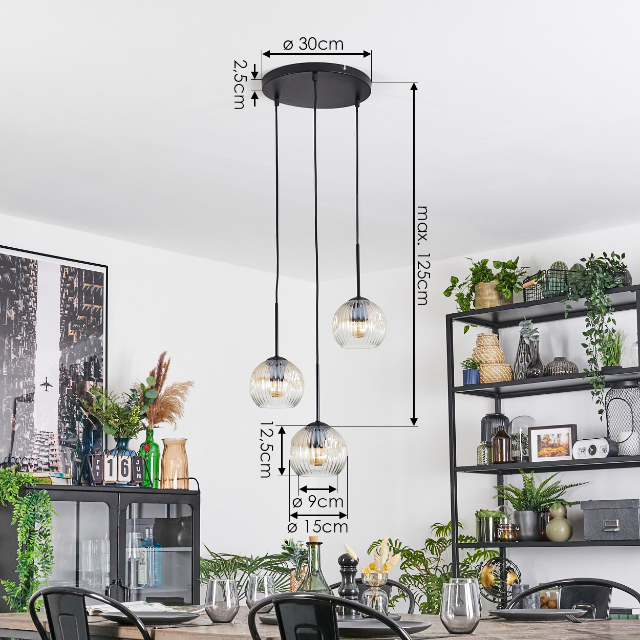 Drei Pendelleuchten mit Glaskugeln hängen über einem Esstisch. Im Hintergrund ein schwarzes Metallregal mit Pflanzen.