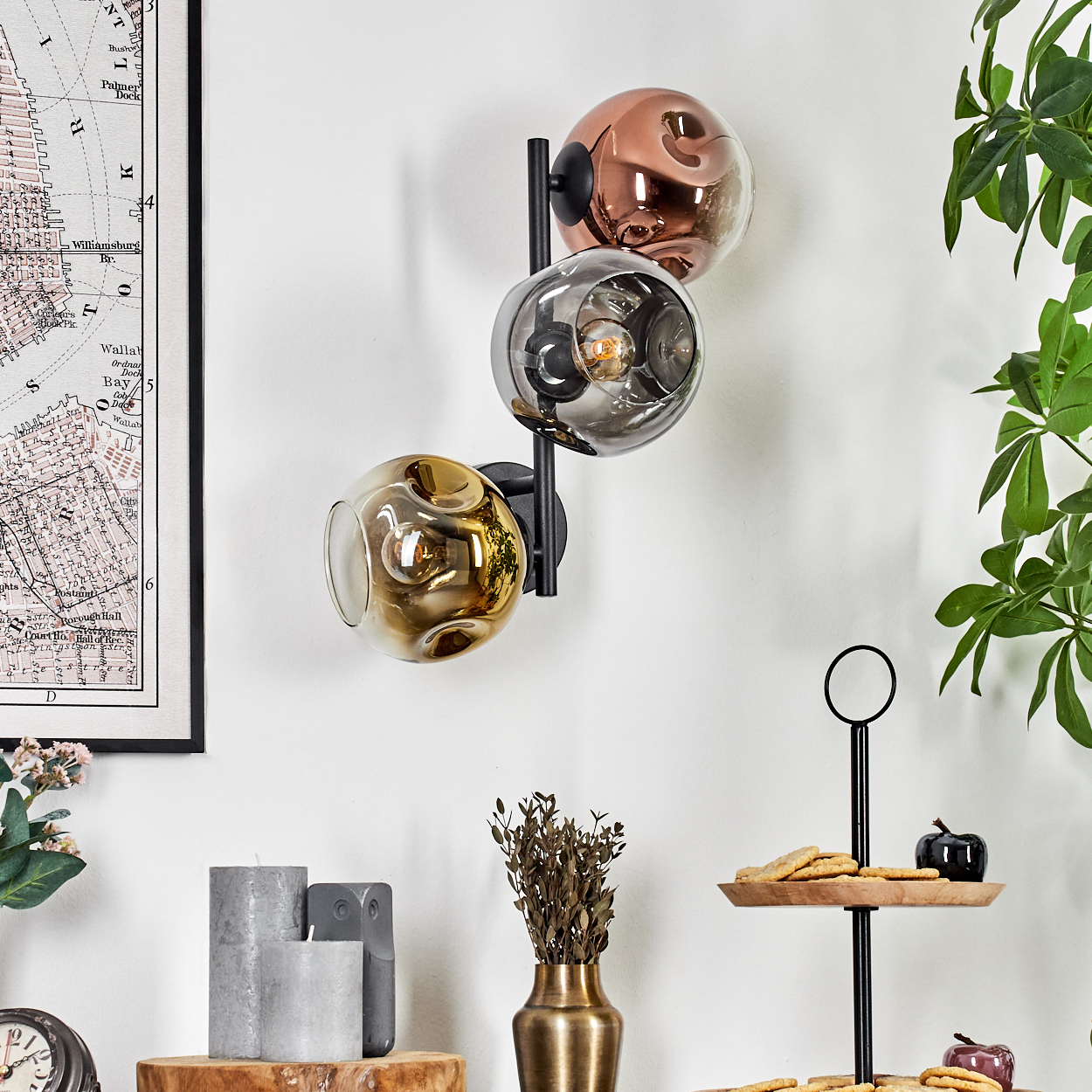 Dreifach-Kugel-Wandlampe, Karte, Kerzen, Vase, Kekse auf einem Ständer und Pflanzen. Die Lampe hat goldene, silberne und kupferfarbene Schirme.