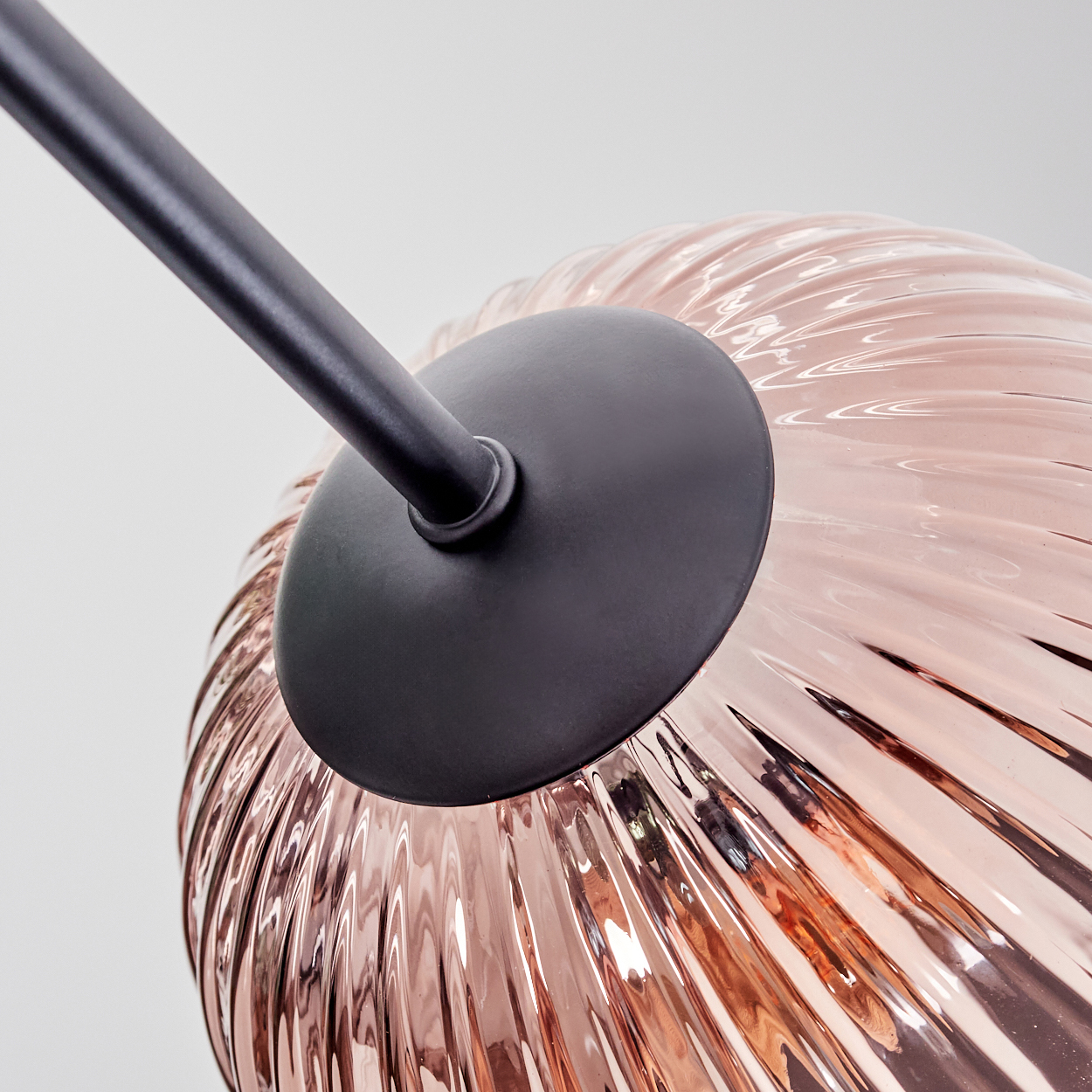Nahaufnahme einer modernen Lampe. Sie hat einen schwarzen Arm und einen runden, strukturierten, rosa-goldenen Glasschirm. Der Hintergrund ist weiß.