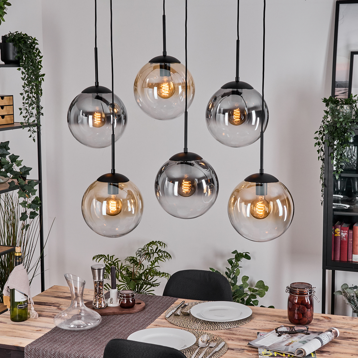 Esszimmer mit sechs hängenden Kugelleuchten. Tisch zum Abendessen gedeckt mit Tellern und einem Einmachglas. Pflanzen sind sichtbar.