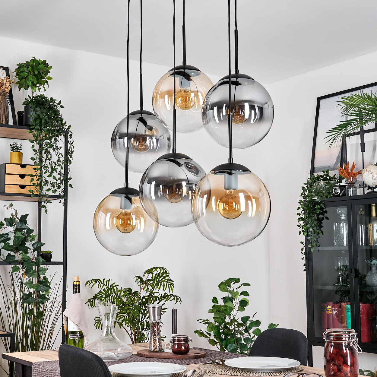 Esszimmer mit sechs Glaskugel-Pendelleuchten. Pflanzen, Holztisch, schwarze Stühle und ein Schrank sind im Hintergrund sichtbar.