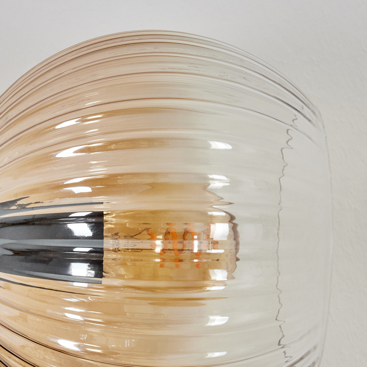 Nahaufnahme einer Glaslampe mit geripptem Design. Die Lampe hat einen Farbverlauf von klar bis bernsteinfarben. Die Glühbirne ist sichtbar.
