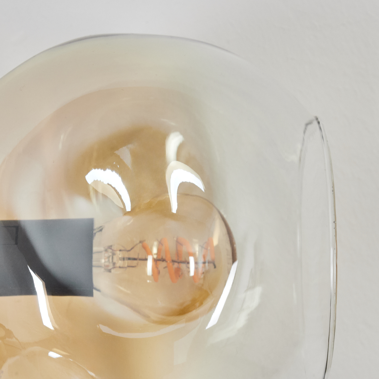 Nahaufnahme einer Leuchte, die eine Glühbirne in einem klaren, runden Glasschirm zeigt. Die Birne hat einen orangefarbenen Wendelfaden.