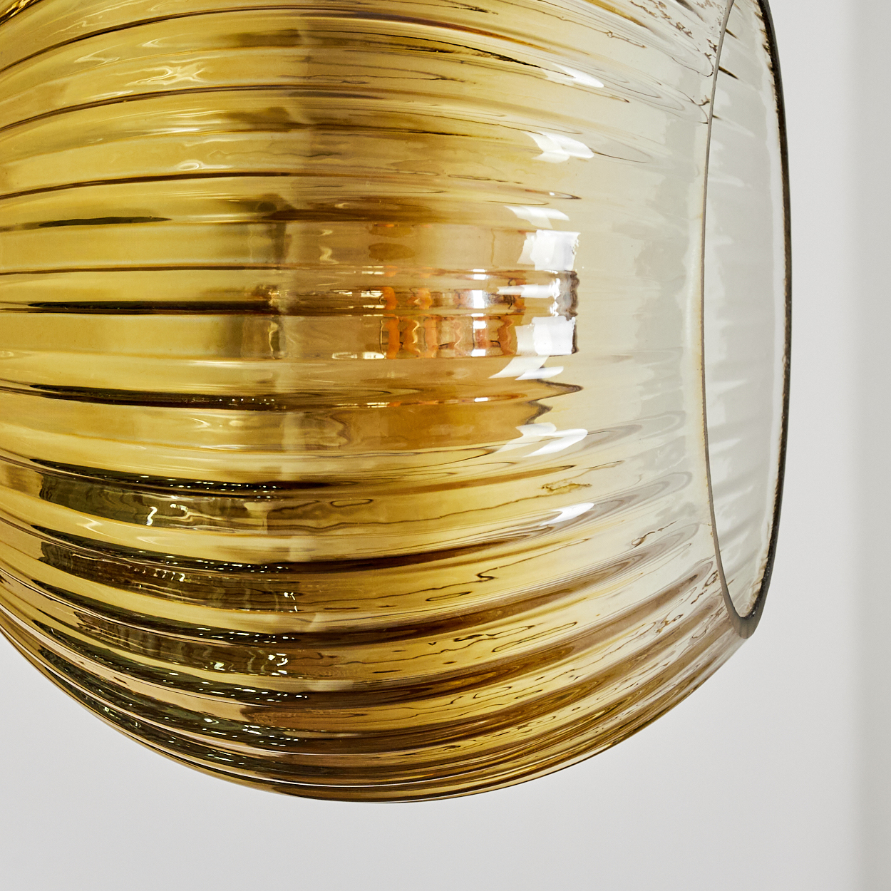Nahaufnahme einer goldenen, gerippten Glaslampe. Licht reflektiert auf der Oberfläche. Der Hintergrund ist weiß.