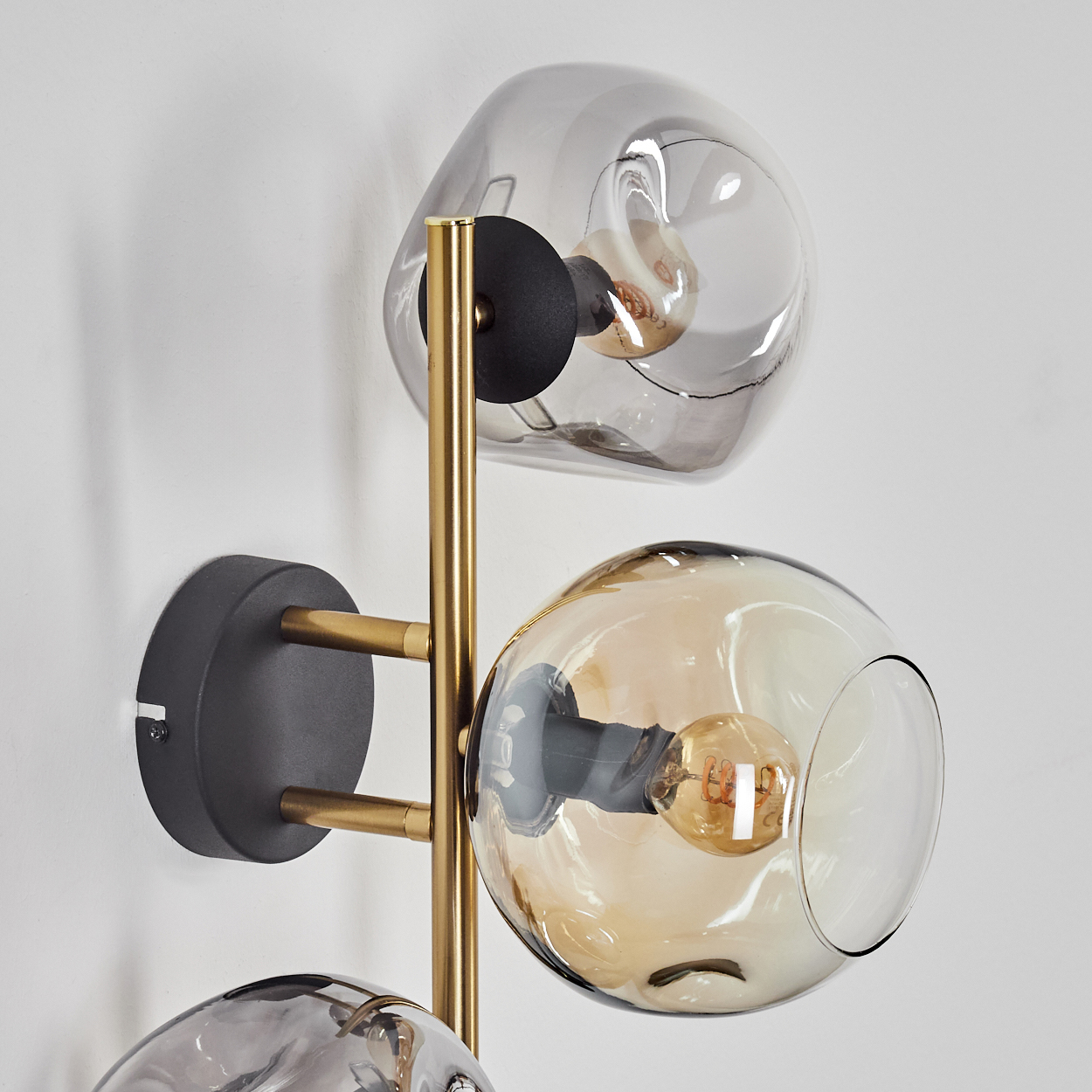 Eine moderne Wandlampe mit drei Glaskugeln. Die Lampe hat einen goldenen Rahmen und einen grauen Sockel. Die Kugeln sind transparent.