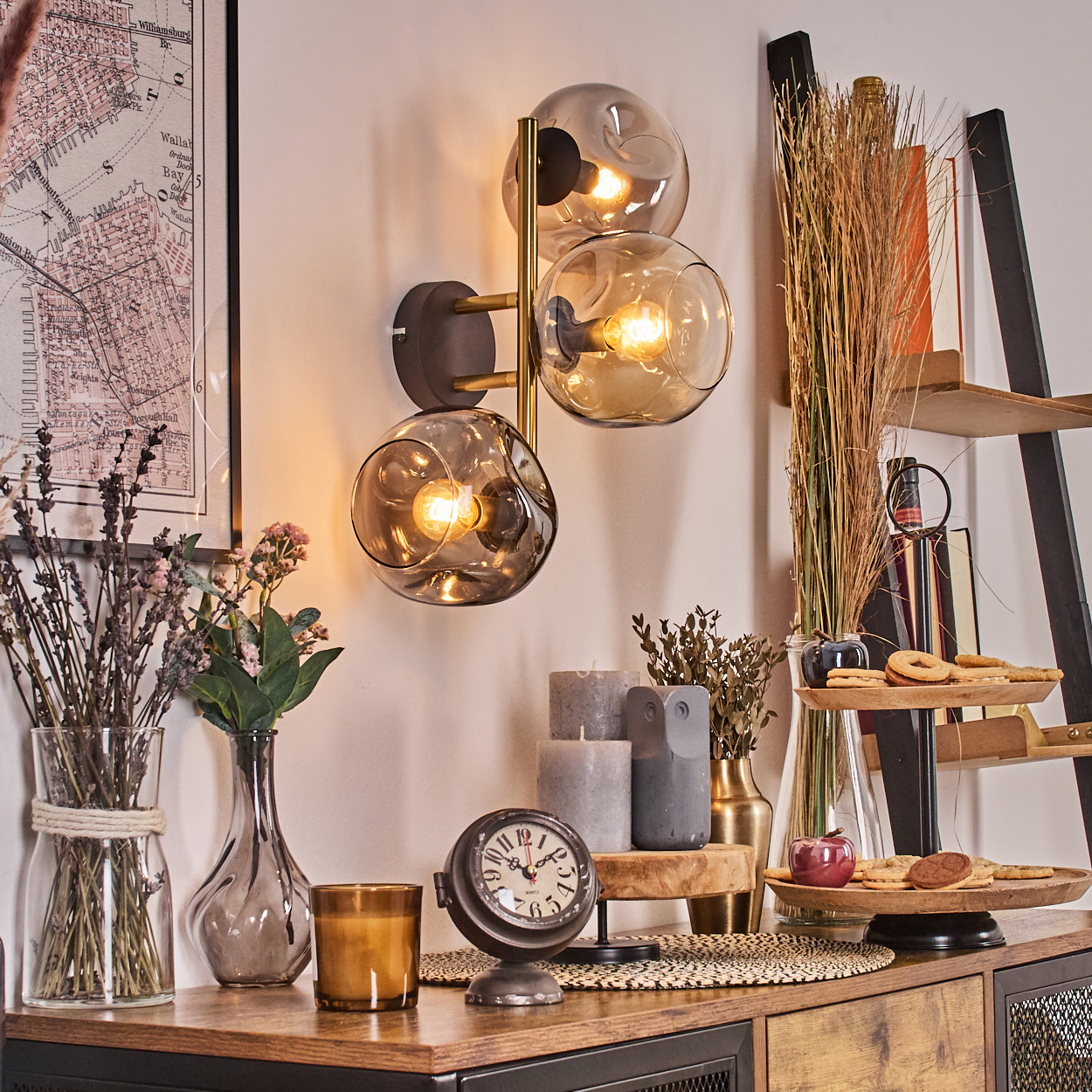 Ein Raum mit Dekoration. Eine Wandlampe, Vasen mit Blumen, eine Uhr, Kerzen und ein Holzregal mit Snacks stehen auf einem Holztisch.