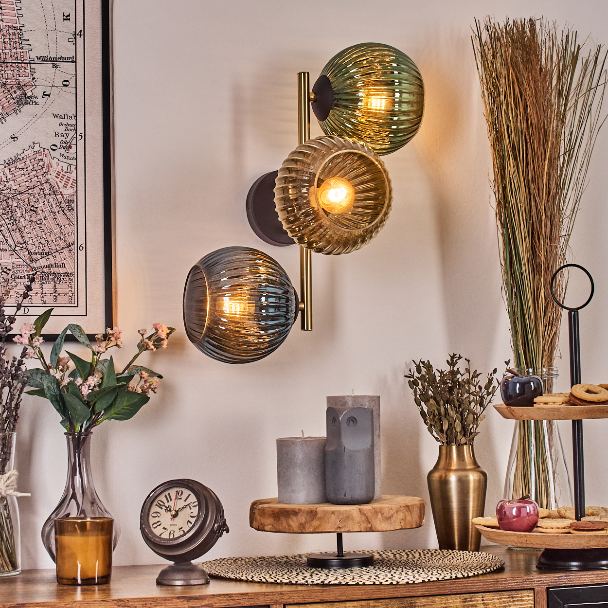 Eine dekorative Wandlampe mit drei Glaskugeln. Verschiedene Gegenstände auf einer Holzoberfläche, einschließlich einer Uhr und Kerzen.
