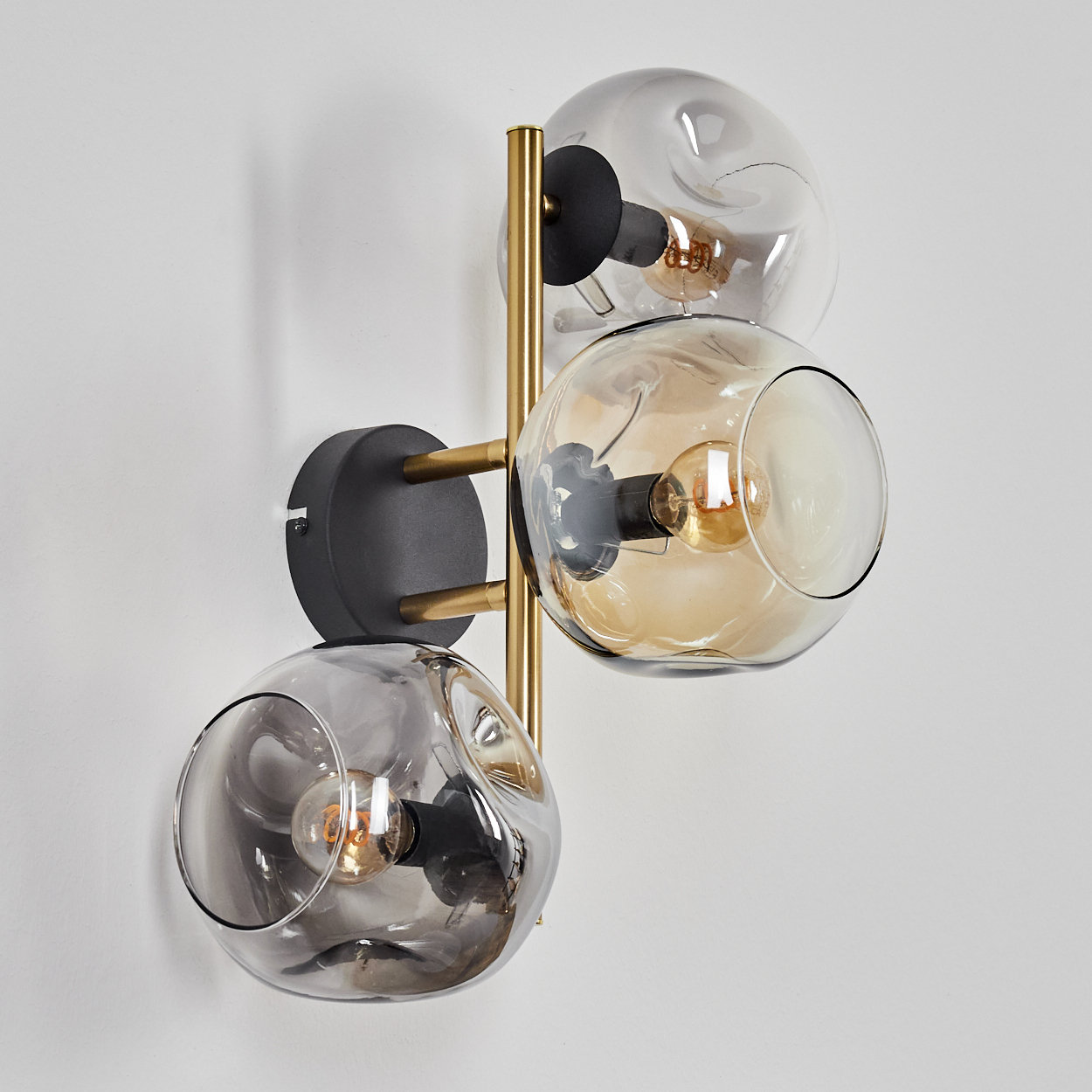 Eine moderne Wandlampe mit drei Glaskugeln, die jeweils eine Glühbirne enthalten. Sie ist an einer weißen Wand montiert.