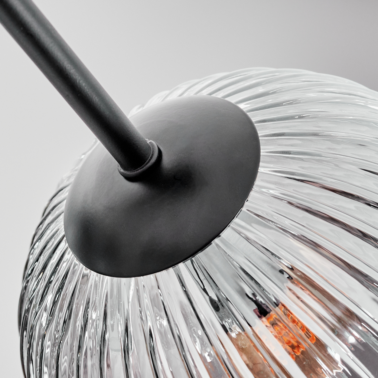 Nahaufnahme einer Glaslampe. Die Lampe hat einen klaren, geriffelten Glasschirm und eine schwarze Metallhalterung.