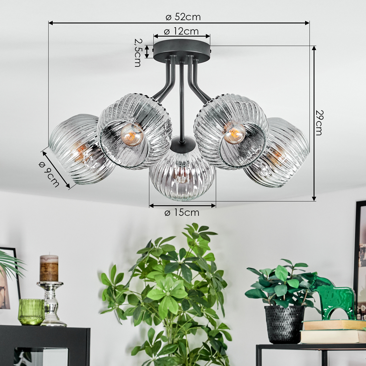 Moderne Deckenlampe mit fünf Glaskugeln, Maße beschriftet. Unten sind Pflanzen und Dekorationsartikel auf einem Regal angeordnet.