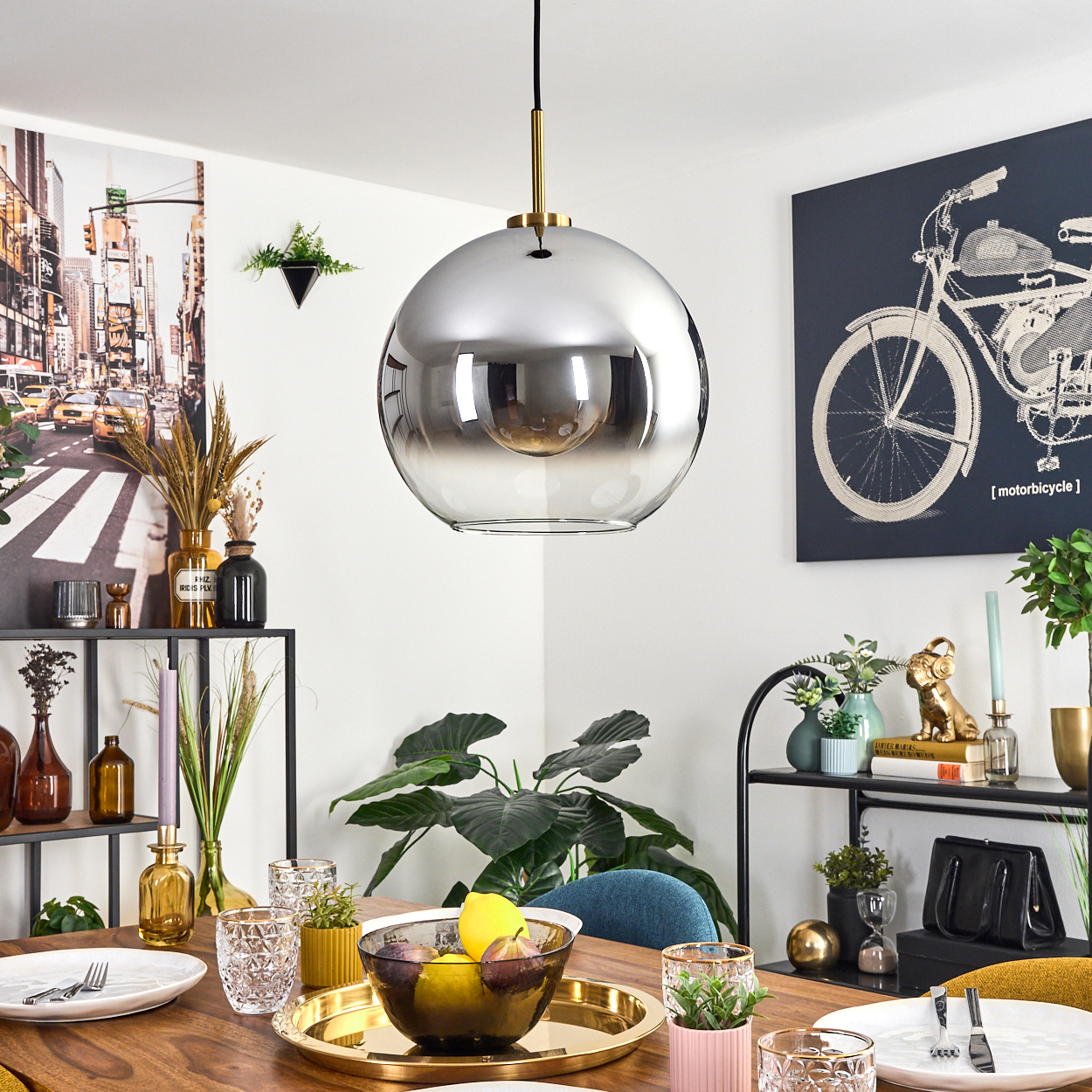 Ein Esszimmer mit einer großen, reflektierenden Kugelleuchte. Ein Tisch ist mit Obst, Pflanzen und Kunst an den Wänden gedeckt.