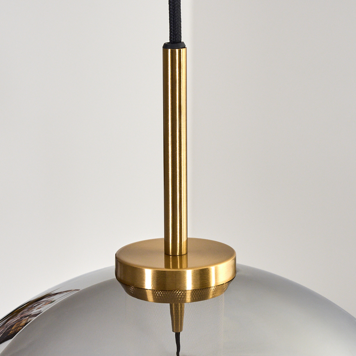 Eine moderne Pendelleuchte mit Metallschirm, Messingdetails und schwarzem Kabel vor schlichtem weißem Hintergrund.