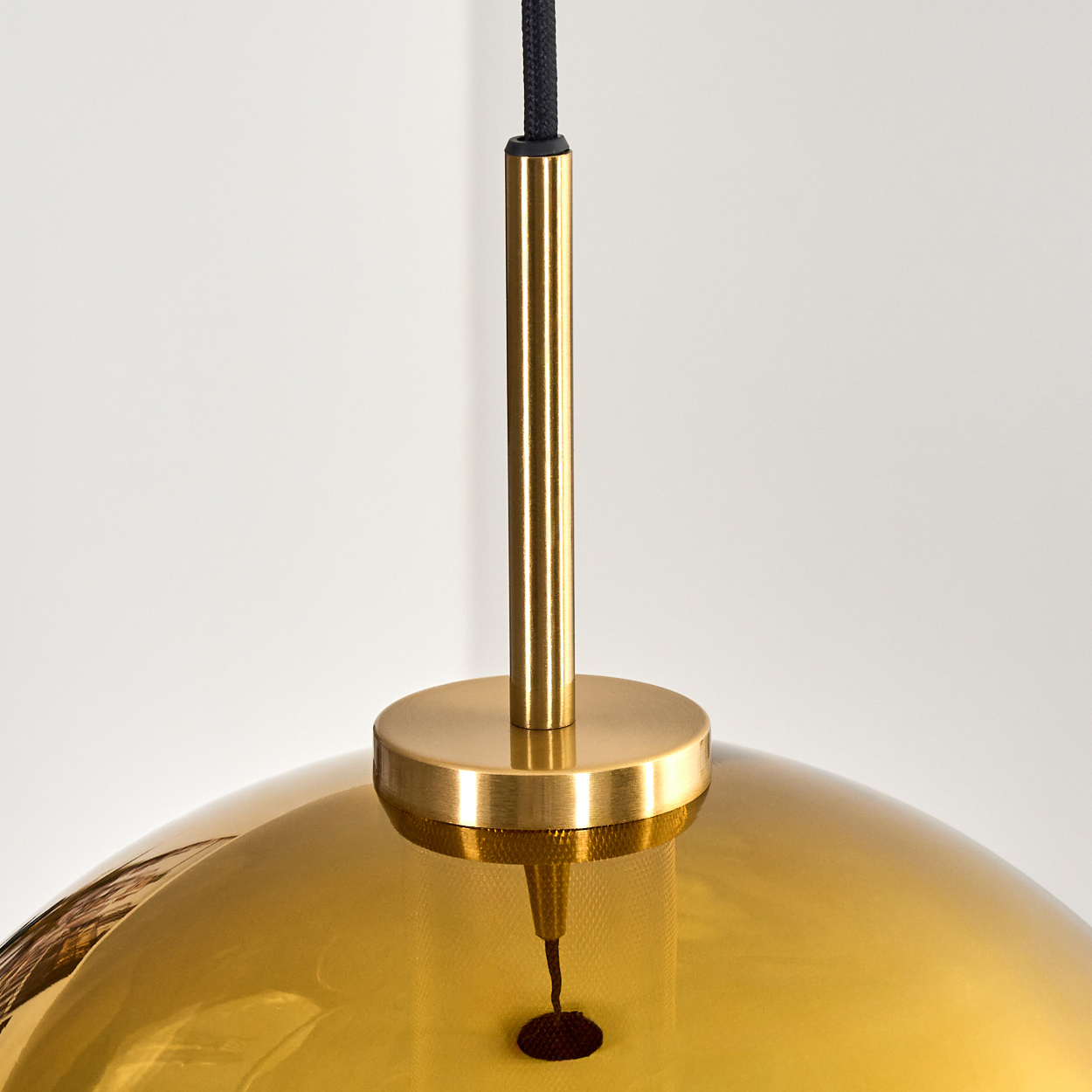 Eine moderne goldene Pendelleuchte mit schwarzem Kabel, zylindrischem Metallschaft und rundem, reflektierendem Lampenschirm vor weißem Hintergrund.