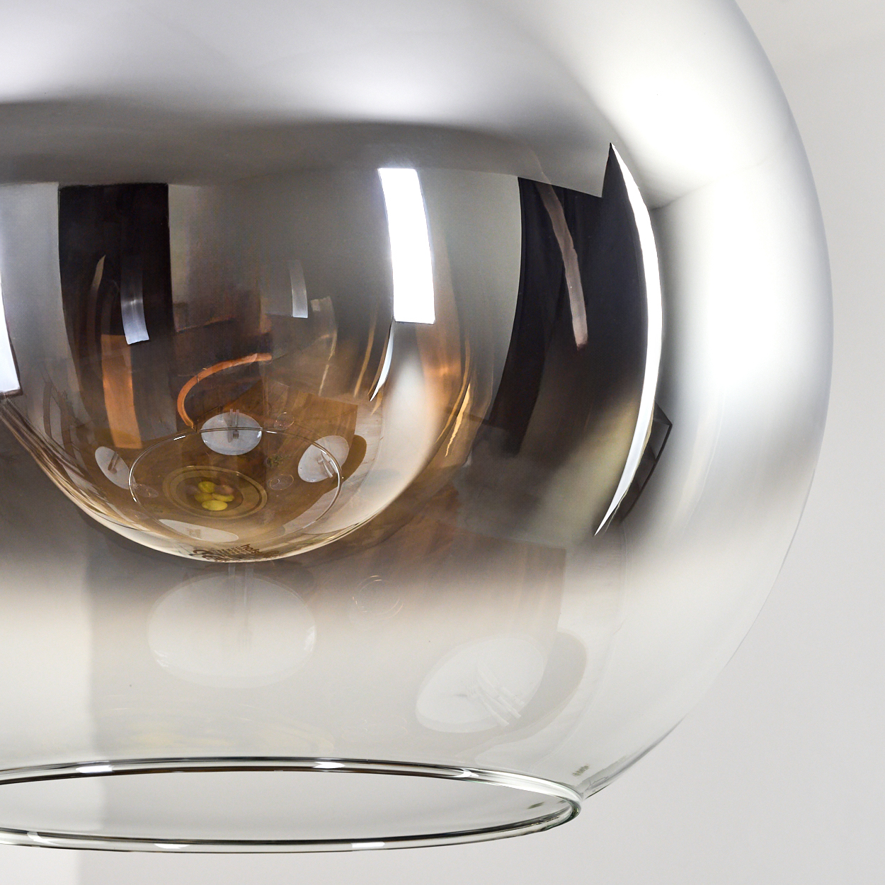 Nahaufnahme einer reflektierenden, kugelförmigen Lampe. Die Lampe reflektiert den Raum, einschließlich Tisch und Leuchten. Die Lampe ist Chrom.